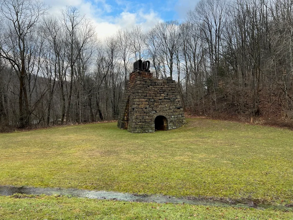 Remains of a stone furnace with an arched opening in a clearing.