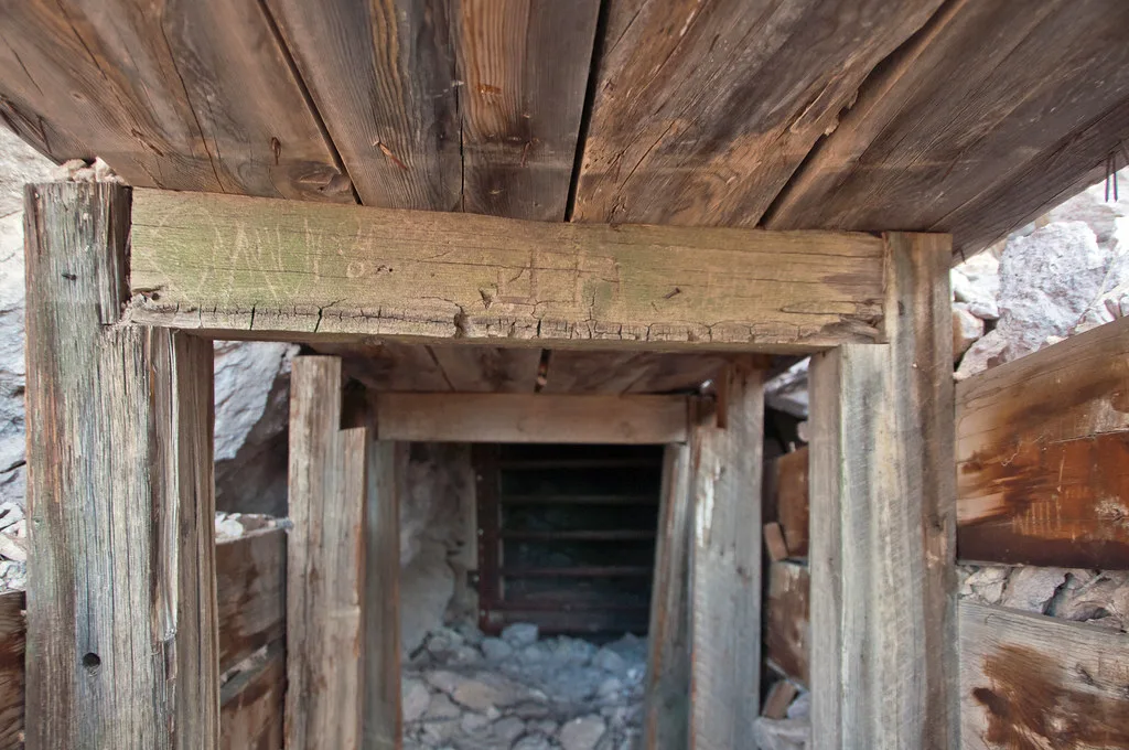 Abandoned gallery entrance with cracked timber supports and a floor covered in fallen rocks.