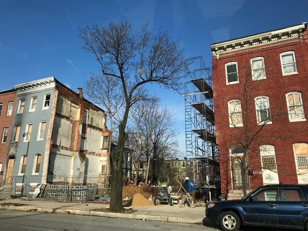 Boarded rowhouses and a demolition site at Wilkens Avenue and Monroe Street in Baltimore.