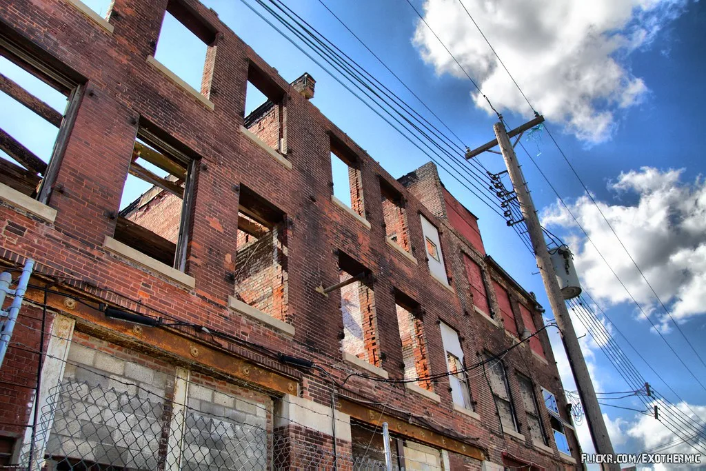 Ruined brick facade with large empty windows beneath clouds.