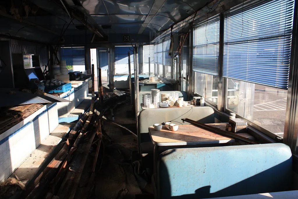 Ancien restaurant aux banquettes bleues et à la vaisselle laissée parmi les débris.