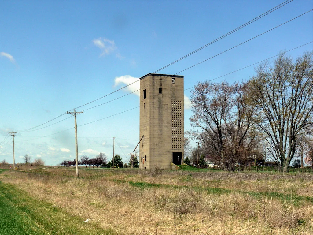 Ancien silo rectangulaire isolé dans une prairie.
