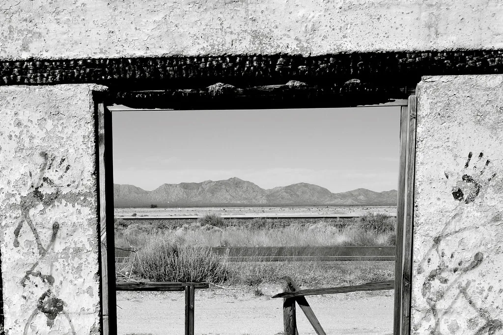 Desert landscape seen through a broken window in a graffiti-covered wall.