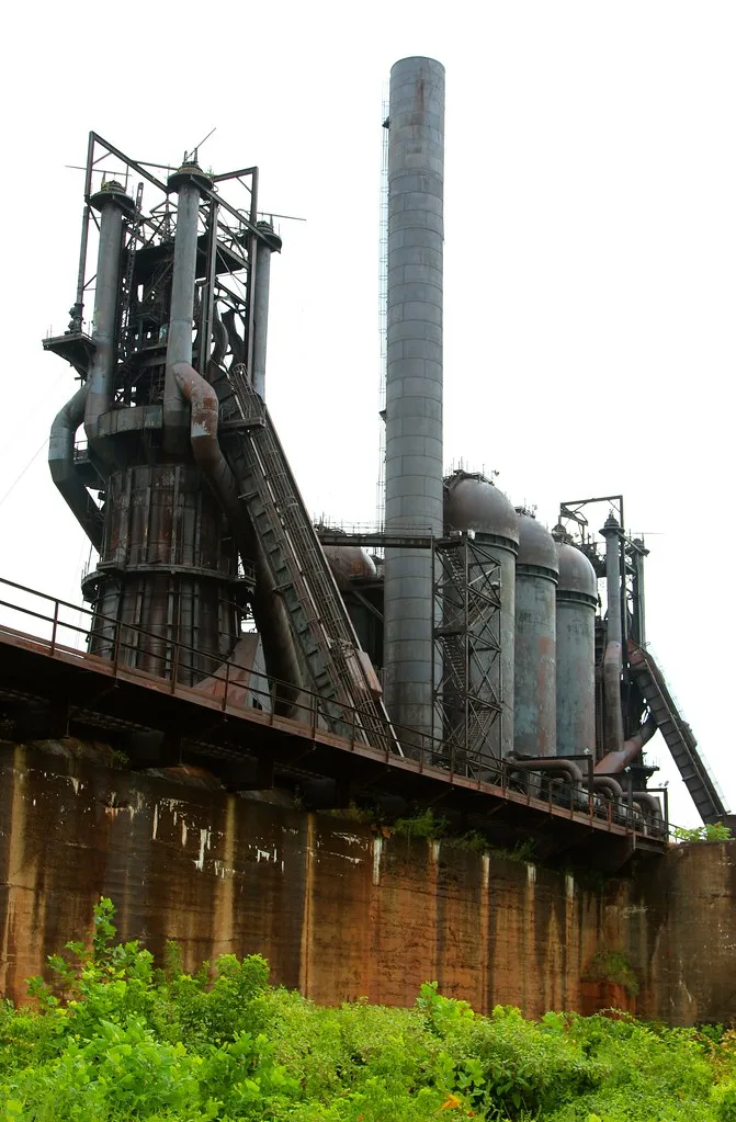 Old rusting industrial installations above a vegetation-covered wall.