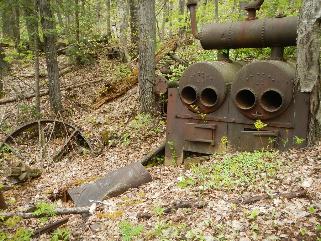 Old rusty boilers and machinery remains in a forest.
