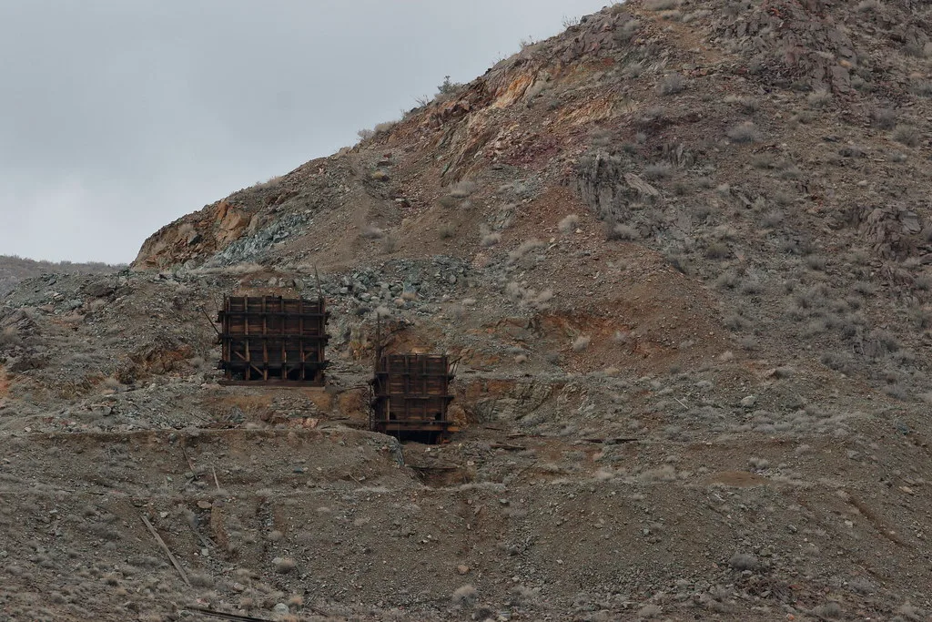 Two old wooden ore chutes at the foot of a rocky slope on a deserted mining site.
