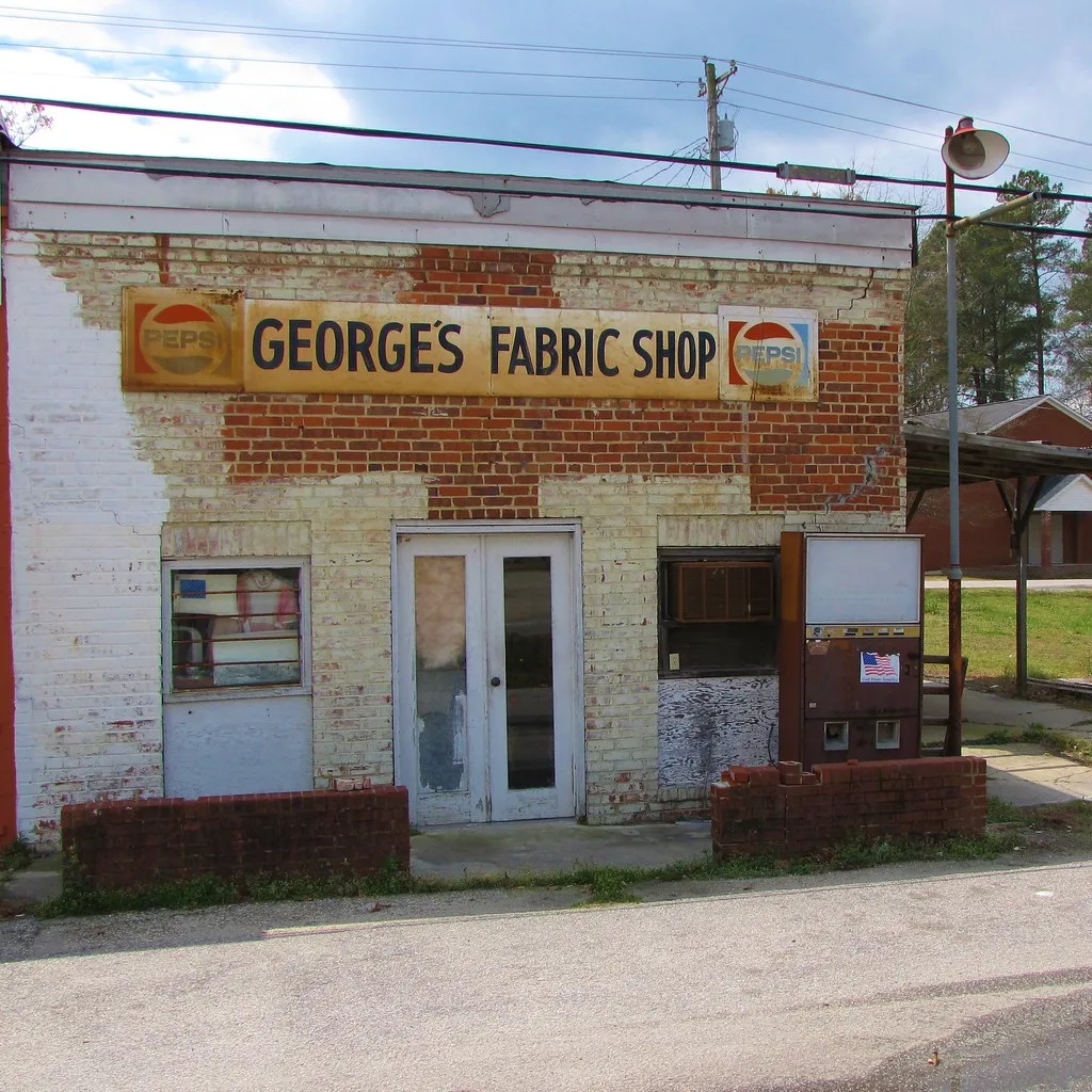 Façade d’une ancienne boutique avec enseigne délavée et distributeur hors usage.