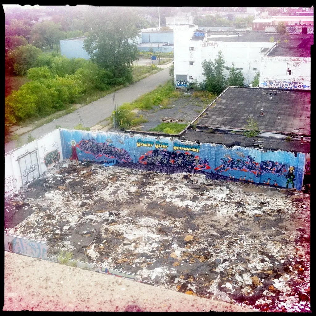 High-angle view of a roofless industrial ruin with rubble-covered ground and graffiti walls.