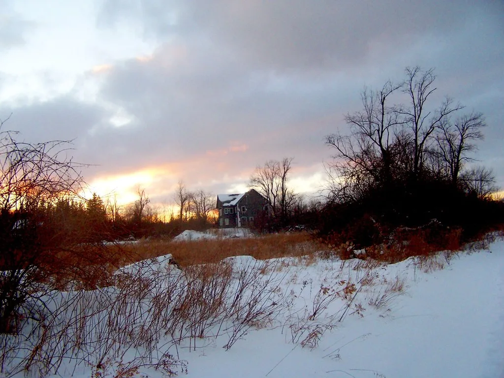Ancienne maison condamnée dans un terrain enneigé au coucher du soleil.