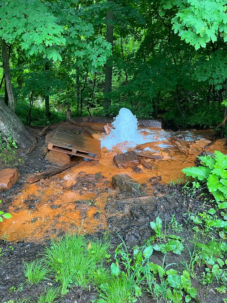 Big Mine Run water jet among orange-stained rocks and vegetation.