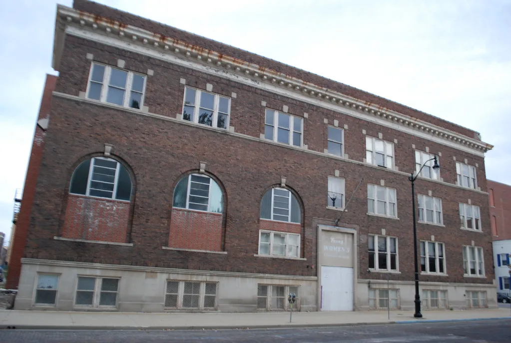 Old brick building with partly broken windows and a boarded main entrance.