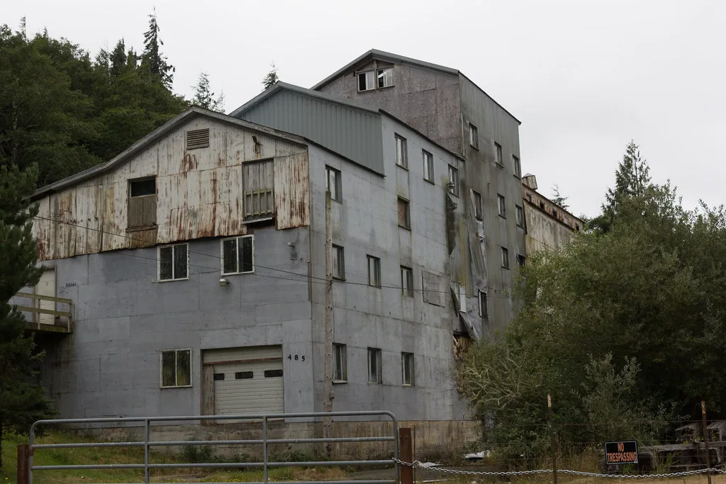 Ancien bâtiment industriel au bardage déchiré derrière un portail fermé.