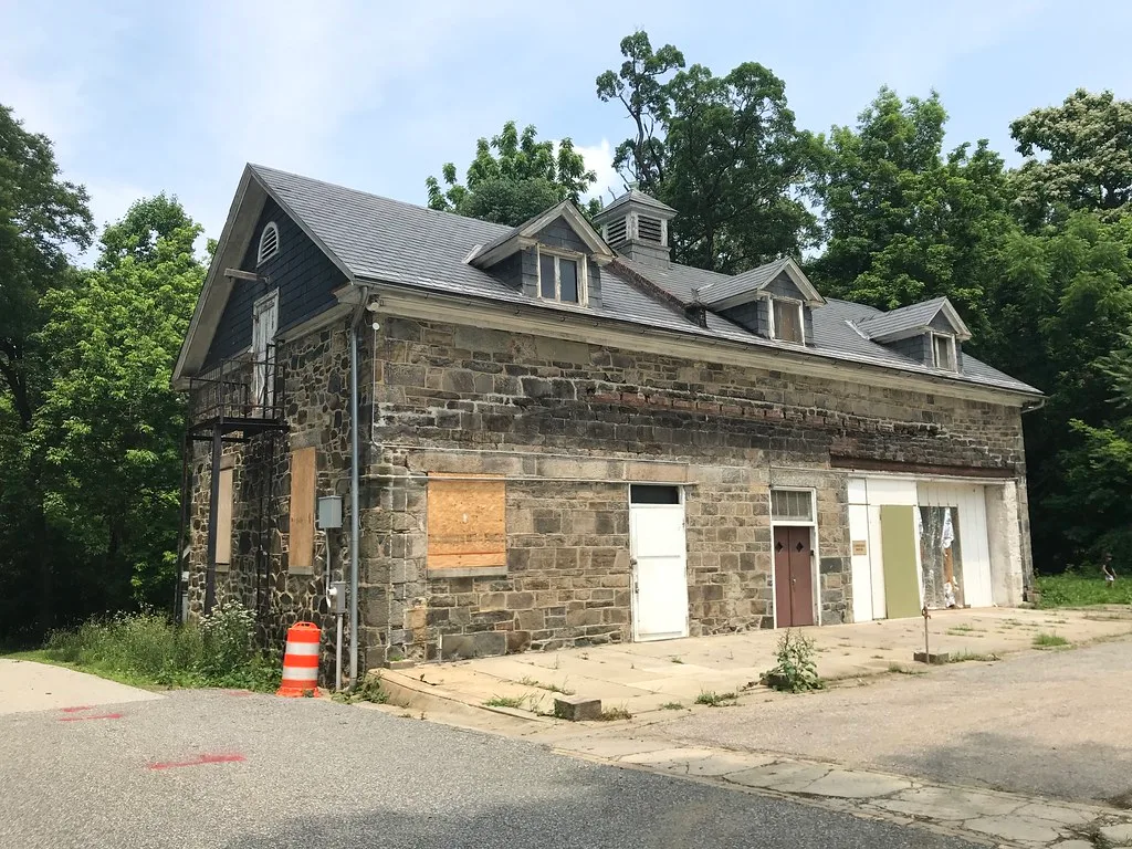 Old stone building with boarded openings beyond cracked paving.
