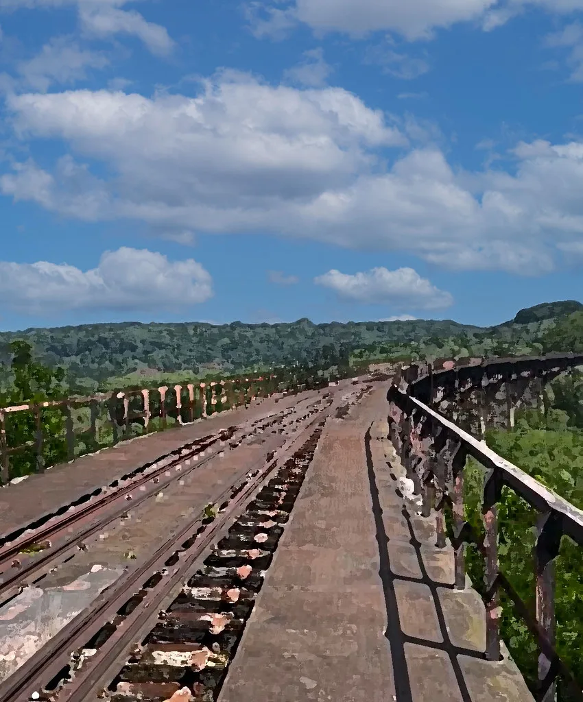 Ancien pont ferroviaire courbe aux traverses dégradées au-dessus d’une vallée boisée.