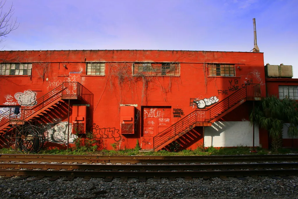 Red graffiti-covered industrial facade with two exterior staircases and broken windows.