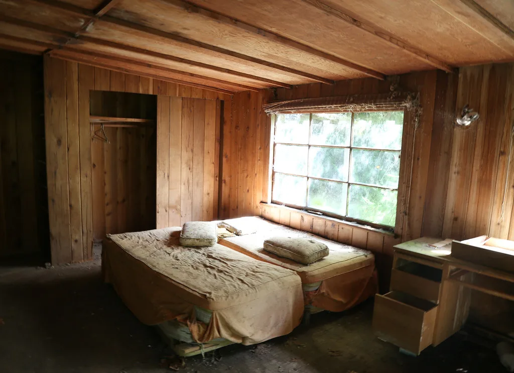 Neglected wood-paneled room with two old mattresses beneath a window.