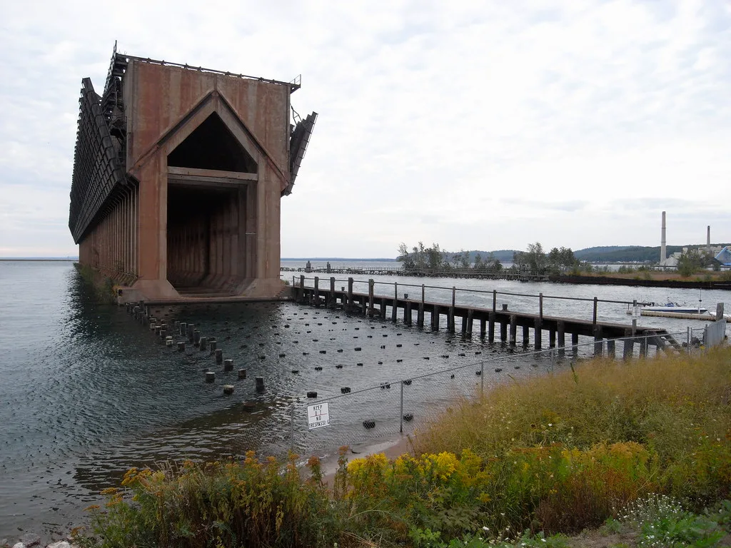 Large abandoned harbor loading structure standing in the water beyond rows of piles with no deck.