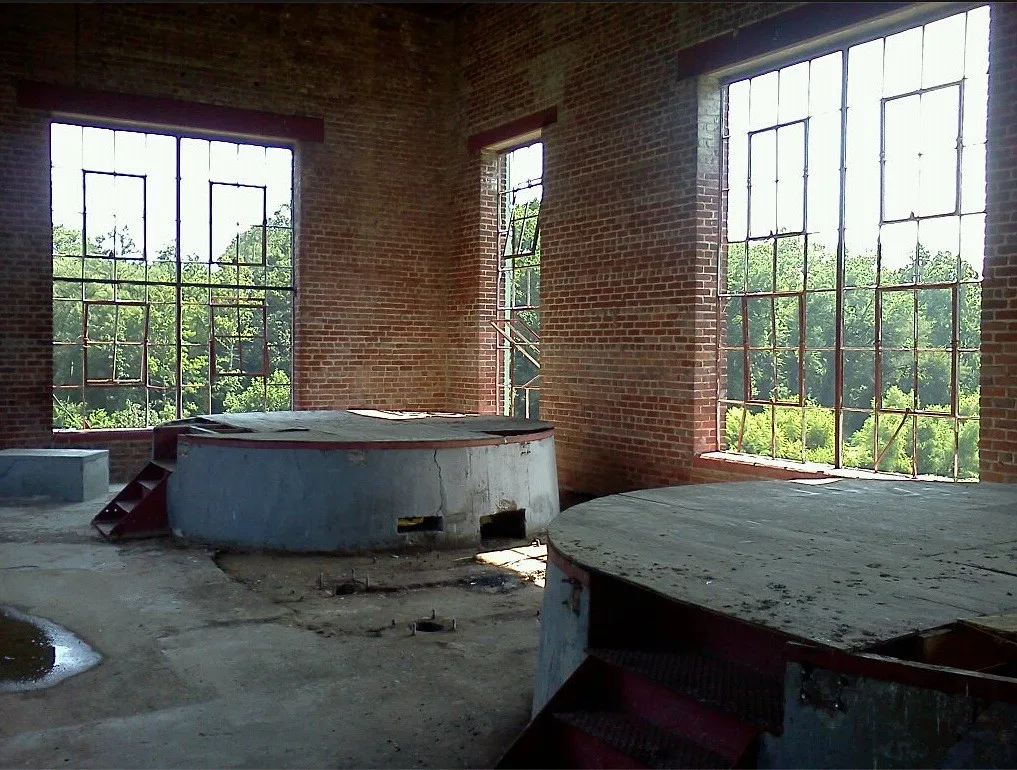 Salle de brique aux fenêtres dépourvues de vitres et à deux grands socles circulaires poussiéreux.