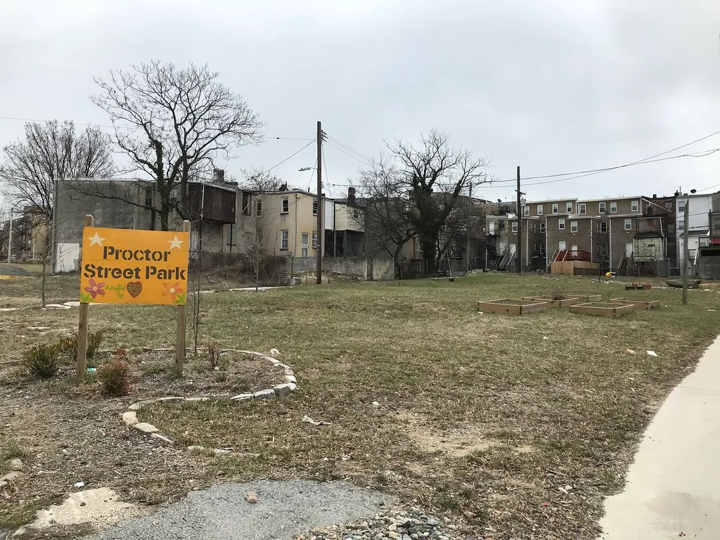 Proctor Street Park à Baltimore, avec son panneau et des parcelles de jardin devant les maisons.