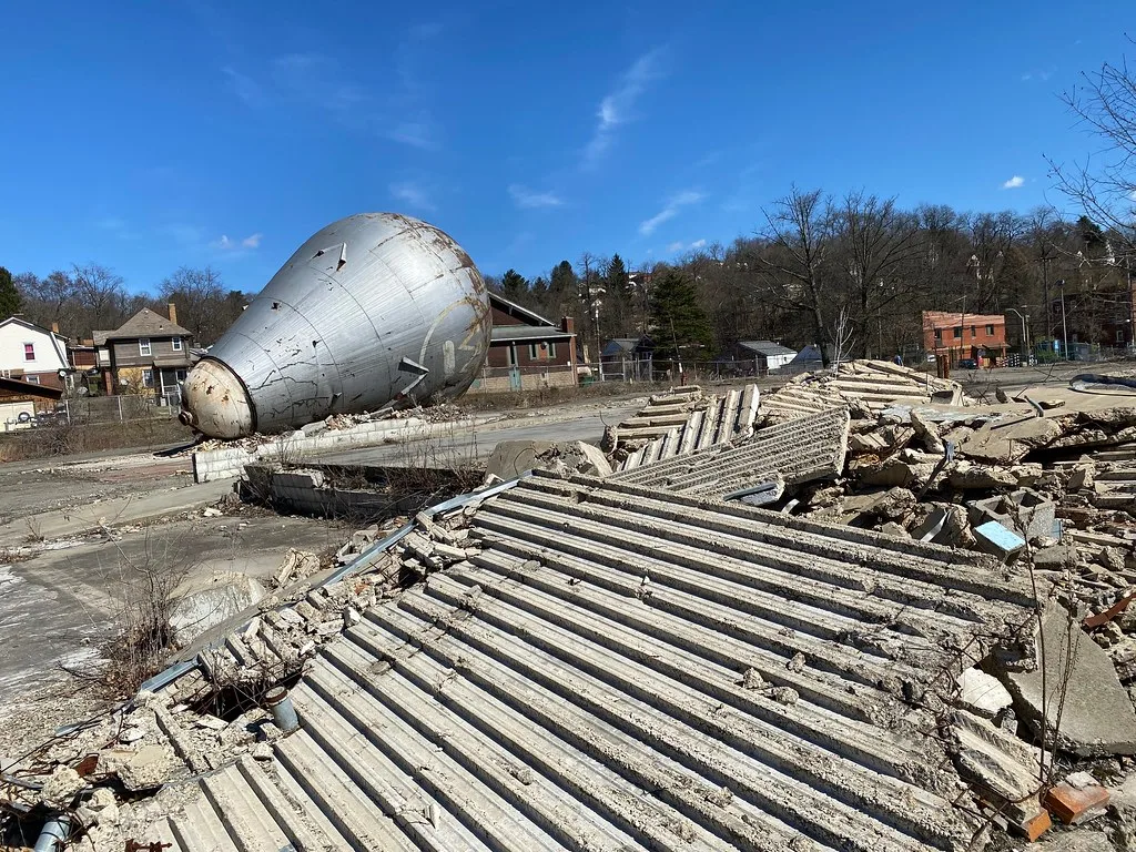 Débris de bâtiment industriel devant une grande structure métallique renversée.