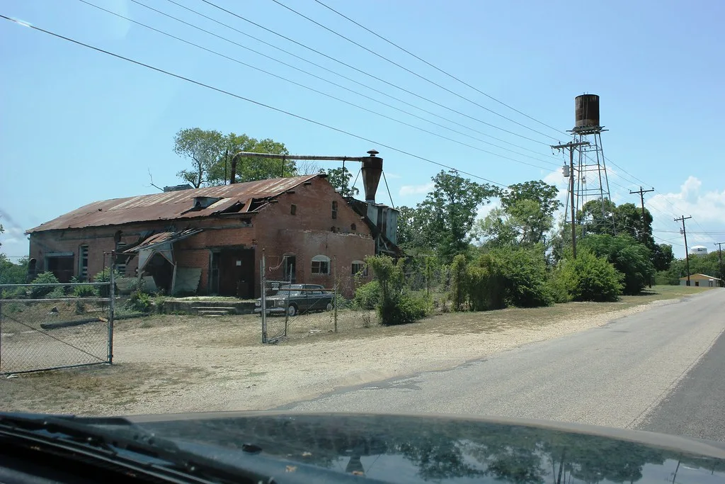 Ancien bâtiment industriel de brique à la toiture trouée près d’un château d’eau.