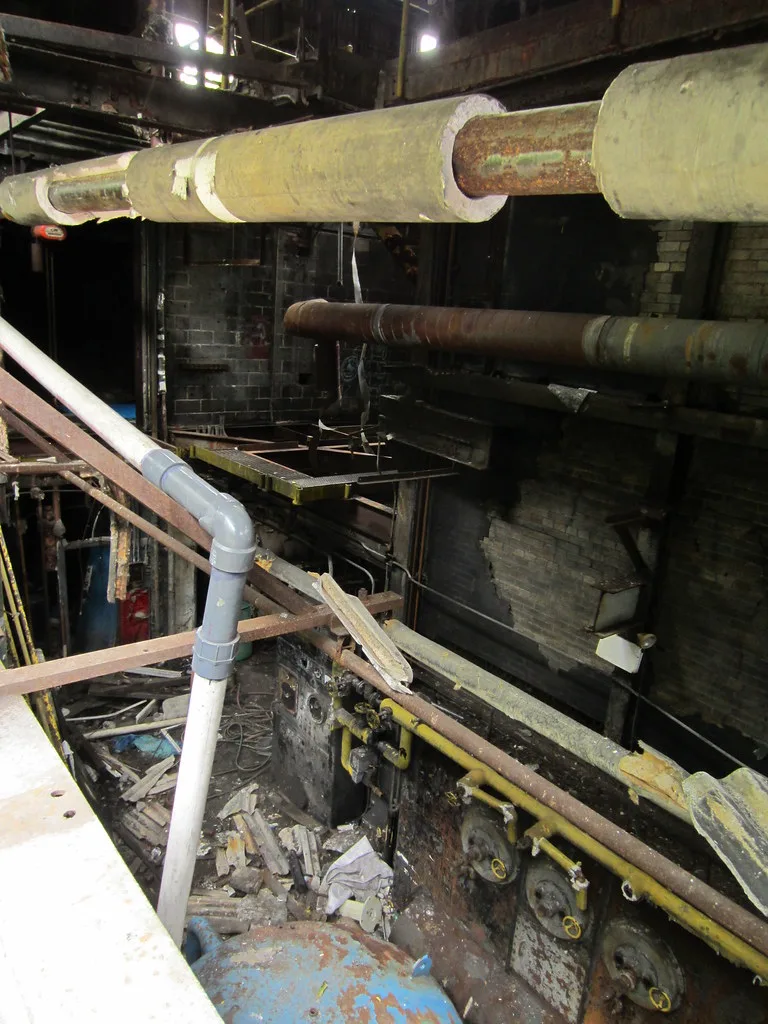 Tuyaux rouillés et équipements dégradés dans un ancien intérieur industriel.