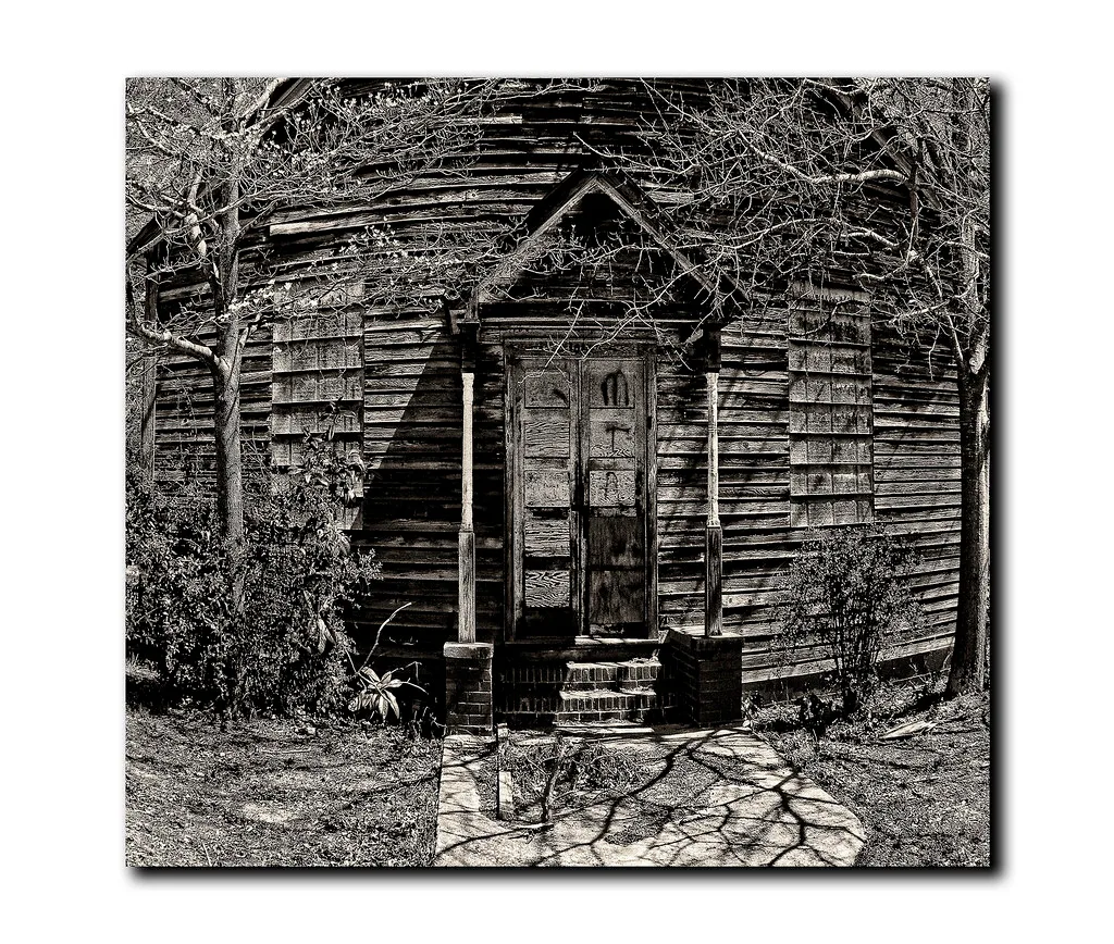 Wooden facade of an old building with boarded windows, in black and white.