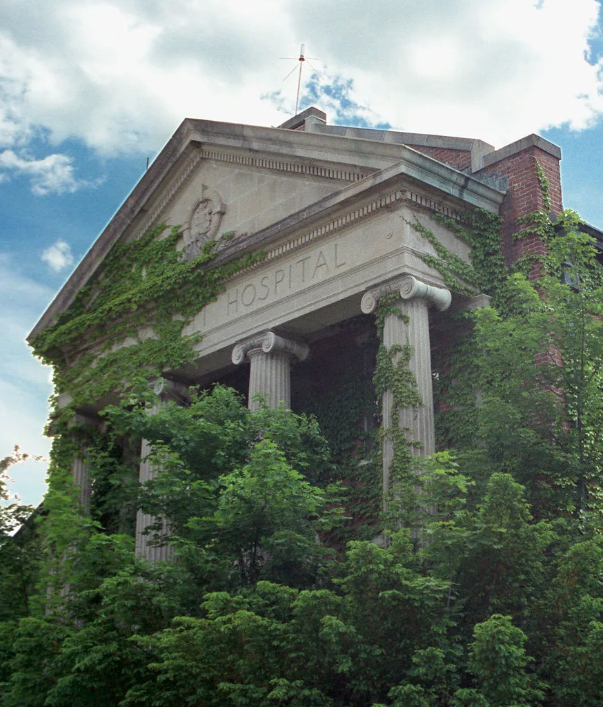 Columned portico of a former hospital overgrown with ivy.