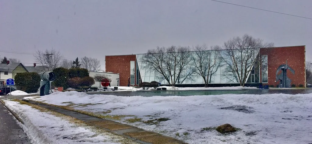 Glass entrance to the University at Buffalo Anderson Gallery in front of a snowy lawn.