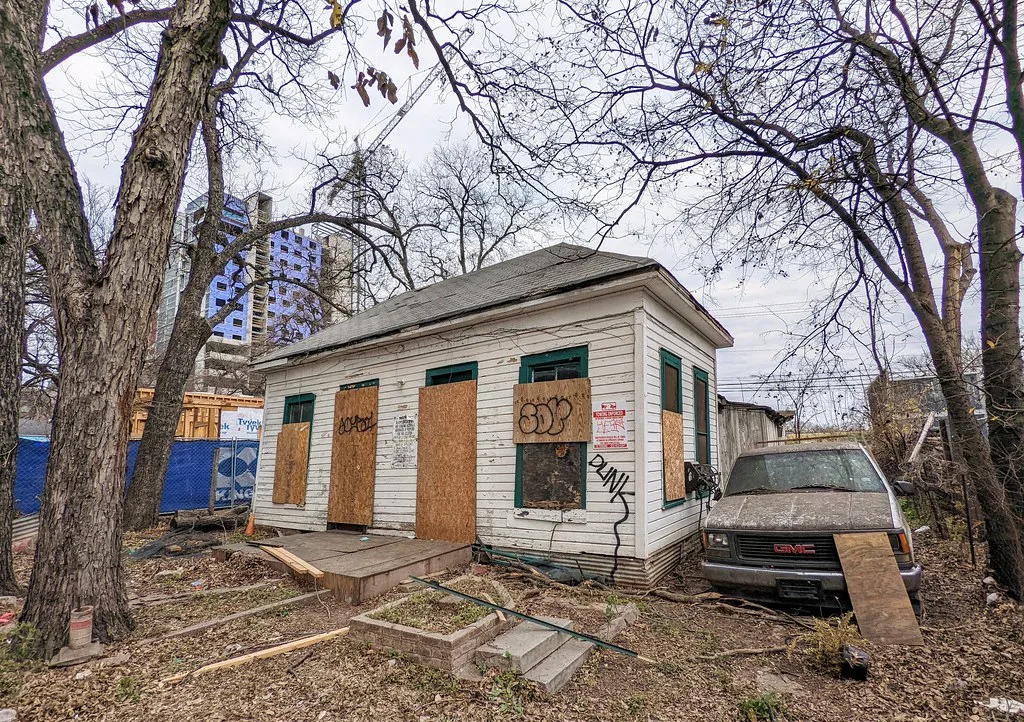 Small boarded white house with removed window frames lying in front.