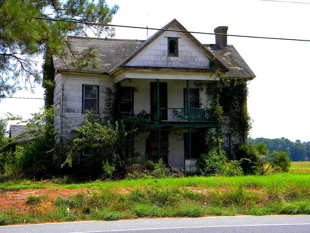 White house with two balconies overgrown with vegetation.