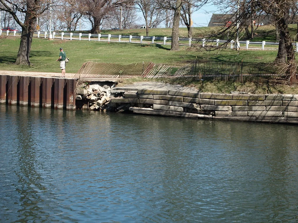 Partly collapsed old stone quay section beside the water.