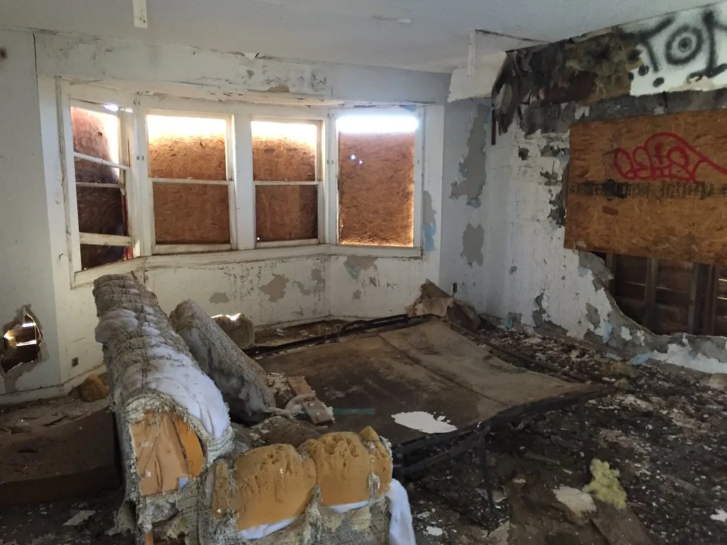 Old interior with boarded windows, a torn sofa and rubble.