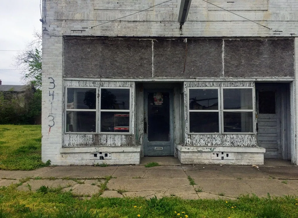 Old white shopfront with peeling paint and its sign removed.