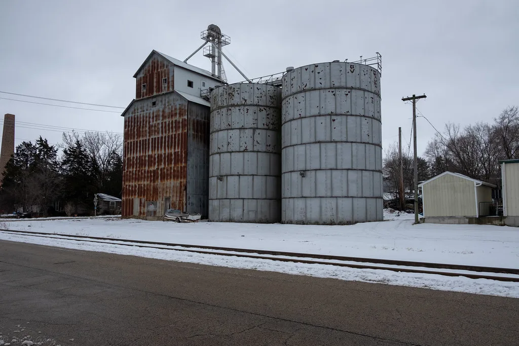 Old rusty grain elevator and white silos on snowy ground.
