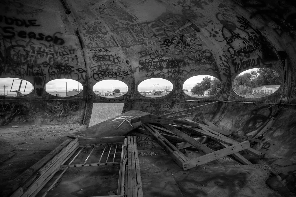 Abandoned interior with oval openings and broken boards beneath graffiti.