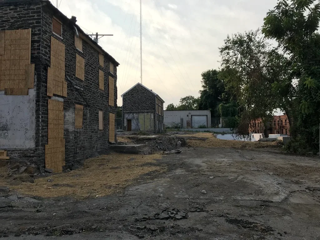 Stone houses with boarded openings around a deteriorated yard.