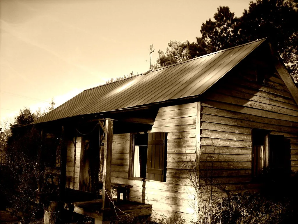 Old wooden house with empty windows and a decayed porch among brush.