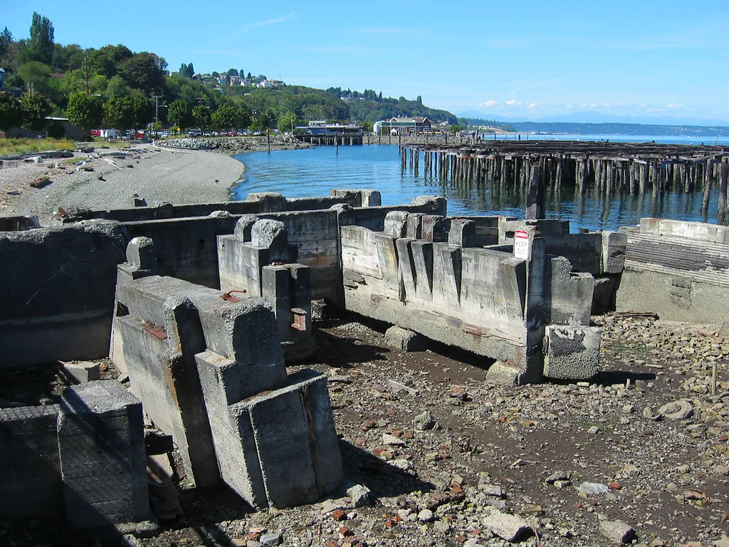 Ruined concrete structures on the shore before the broken piles of an old wharf.