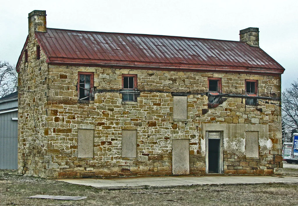 Ancienne maison de pierre aux baies condamnées sous une toiture métallique rouge.