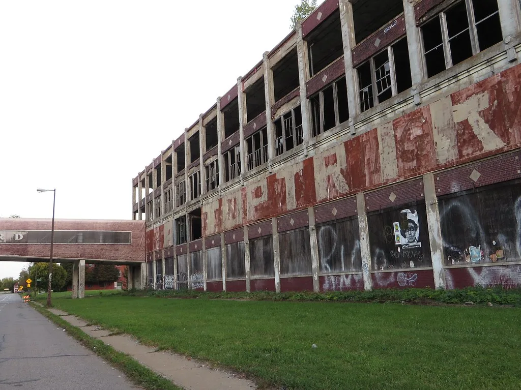 Abandoned factory facade with empty windows and faded painted lettering, connected to a walkway over the street.