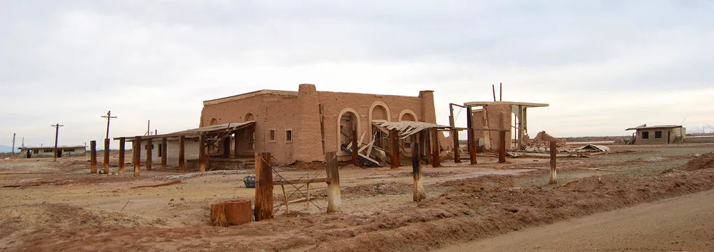 Old masonry building with collapsed canopies on arid ground.