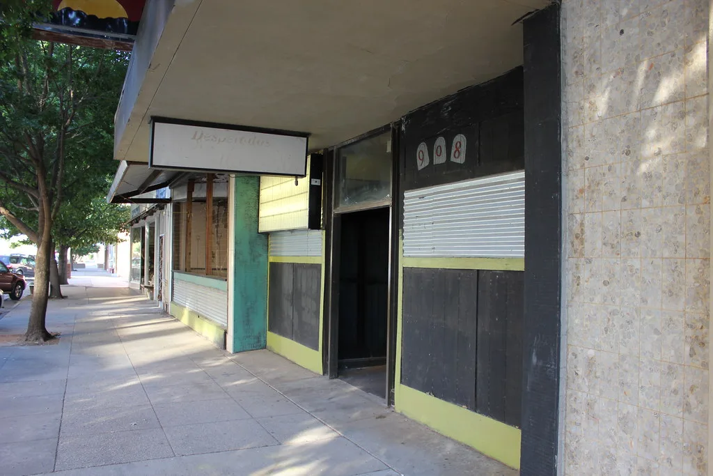 Former shopfronts with boarded openings along a pavement.