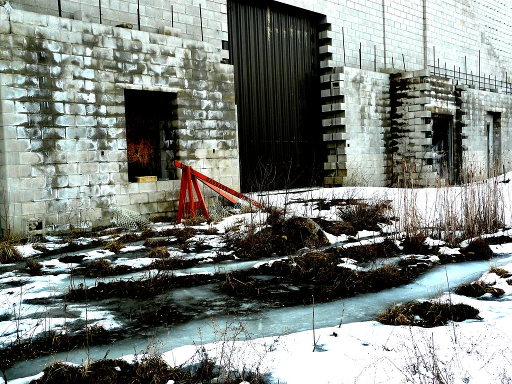 Old blockwork facade with empty openings above a snowy, overgrown slab.