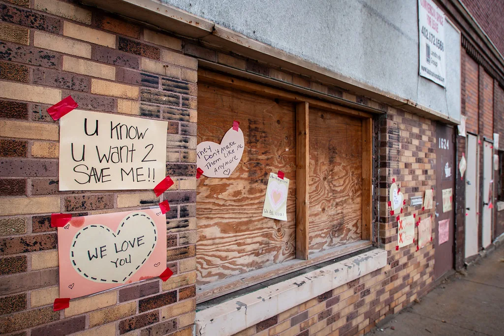 Boarded window of an old brick building bearing preservation messages.