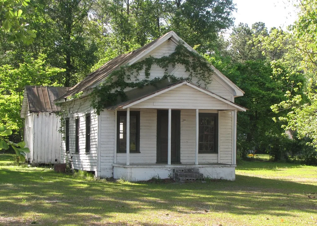 Old white wooden building with a small porch and climbing plants.