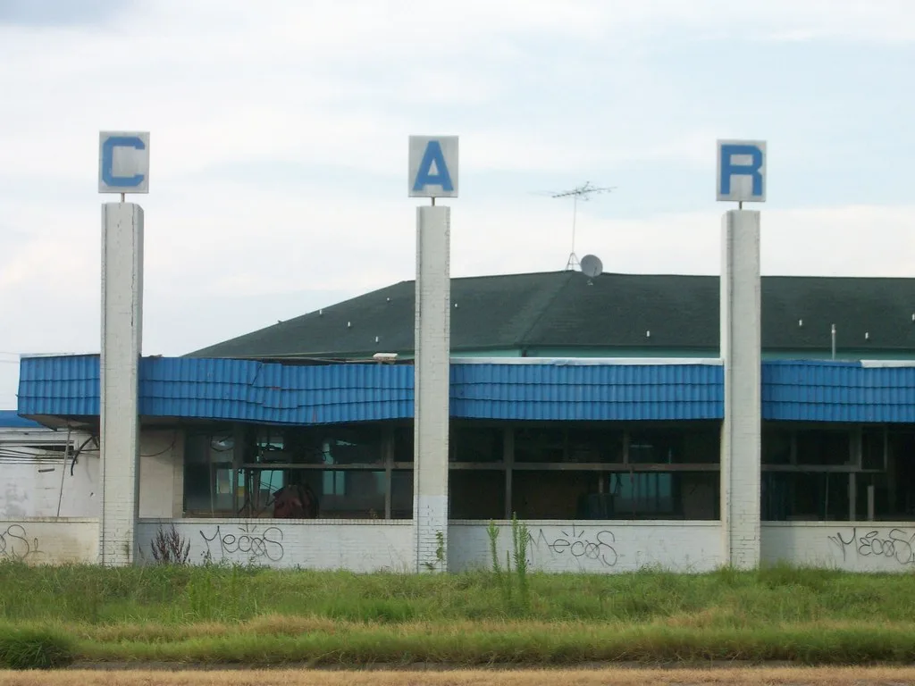 Ancienne station de lavage aux vitres brisées et à la façade bleue, dans les herbes.