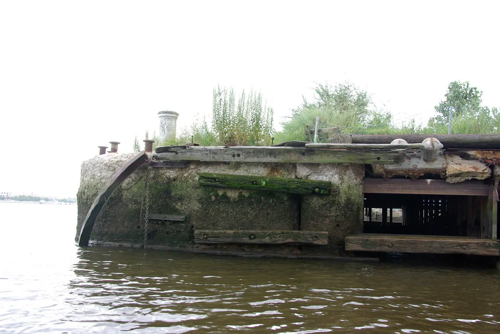 Deteriorated old pier beside the water with vegetation growing on top.