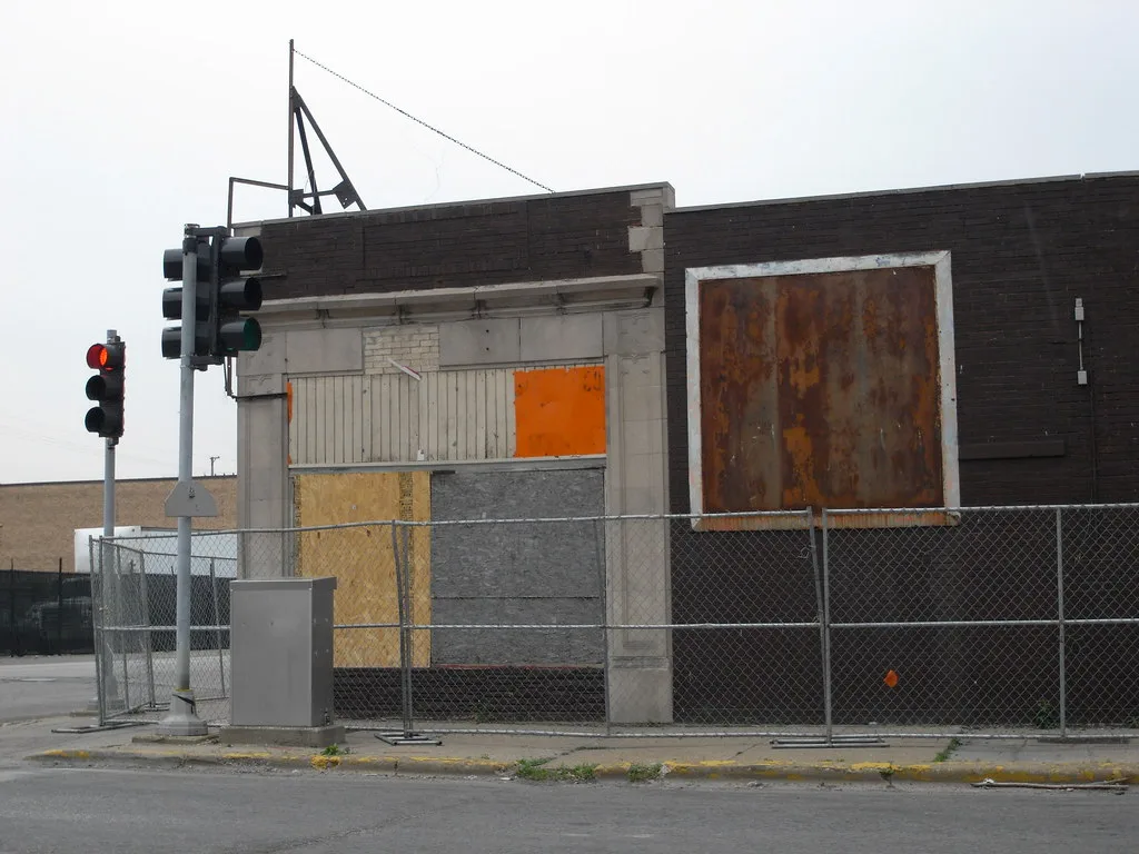 Old building with large boarded openings behind a fence.