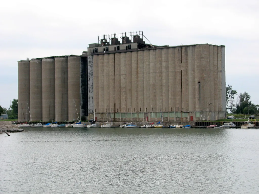Abandoned old waterfront silos with deteriorated upper structures behind moored sailboats.